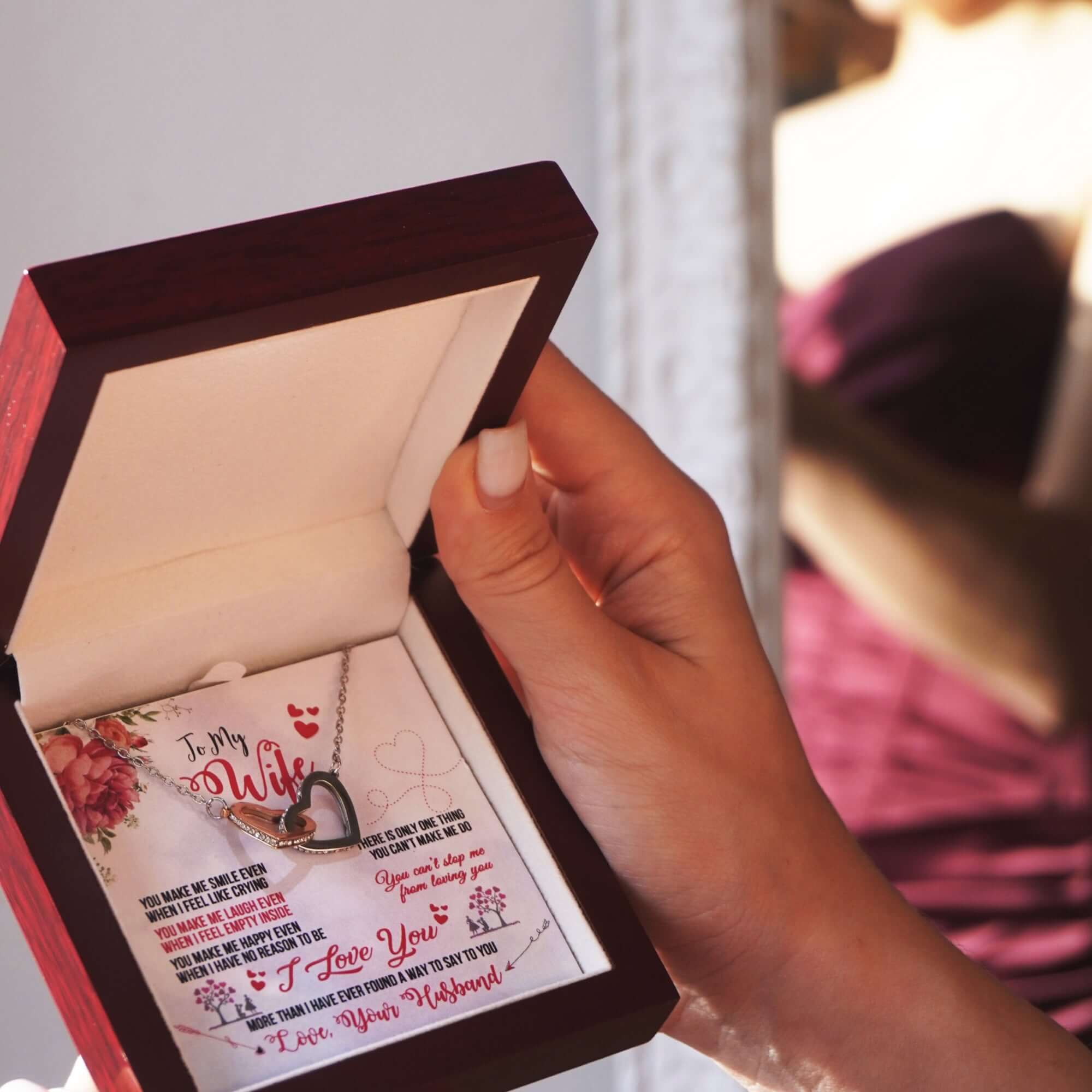 Hand holding a necklace with a heart design and a card in an open jewelry box.