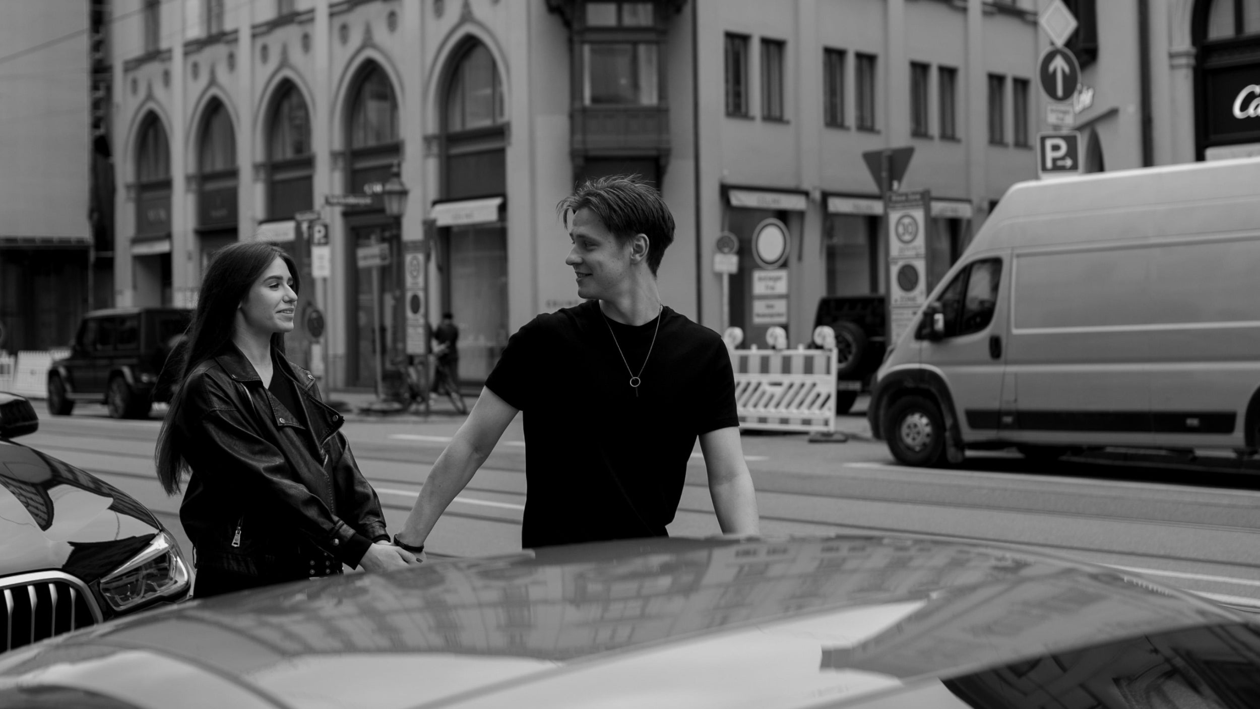 Two people sitting on a car in an urban street setting