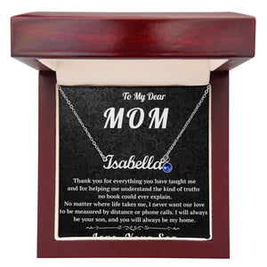 Necklace with a blue gemstone in a wooden box with a personalized message for 'Mom'.