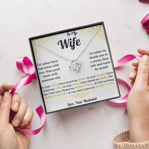 Necklace with heart pendant and sentimental card held by hands with pink ribbons on a light background